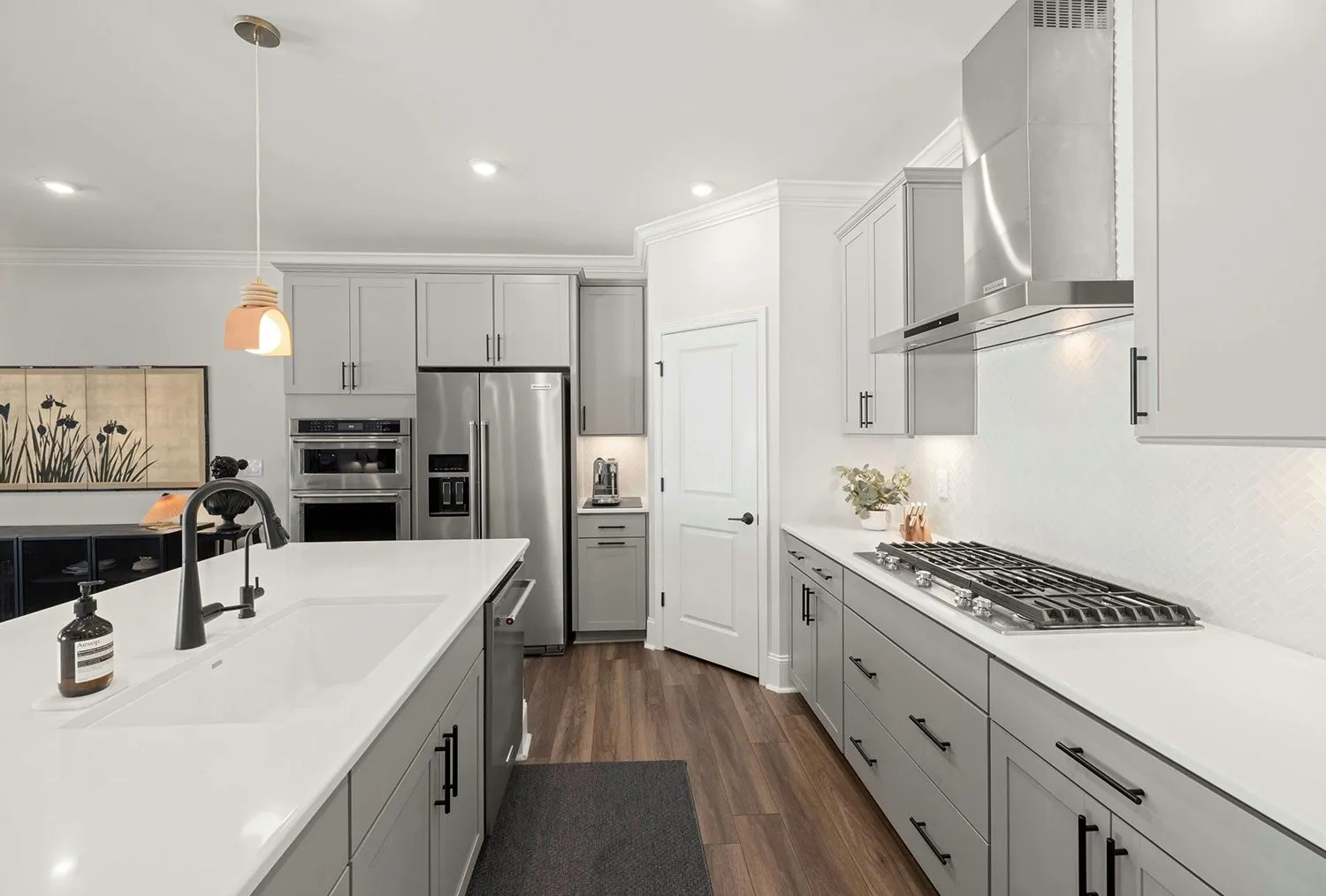 Bright modern kitchen with white cabinets, gray drawers, island, stainless steel appliances, and wood floors